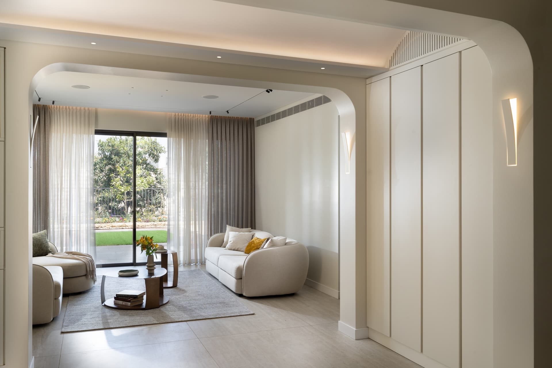 Living room seen through a wide plaster arch, with sheer curtains and garden light beyond