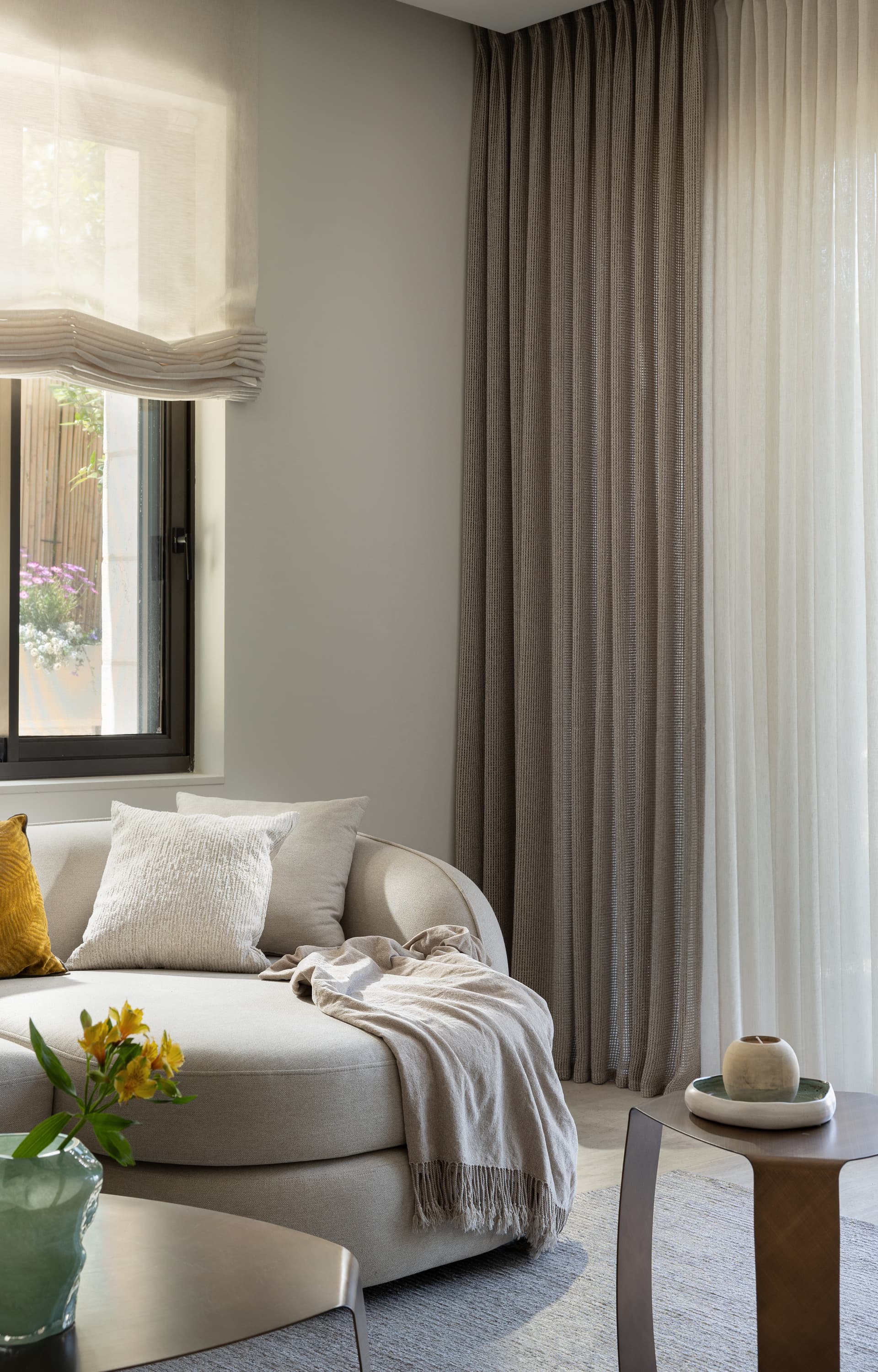 Curved cream sofa with linen pillows, draped throw, and sheer curtains framing a planted garden view