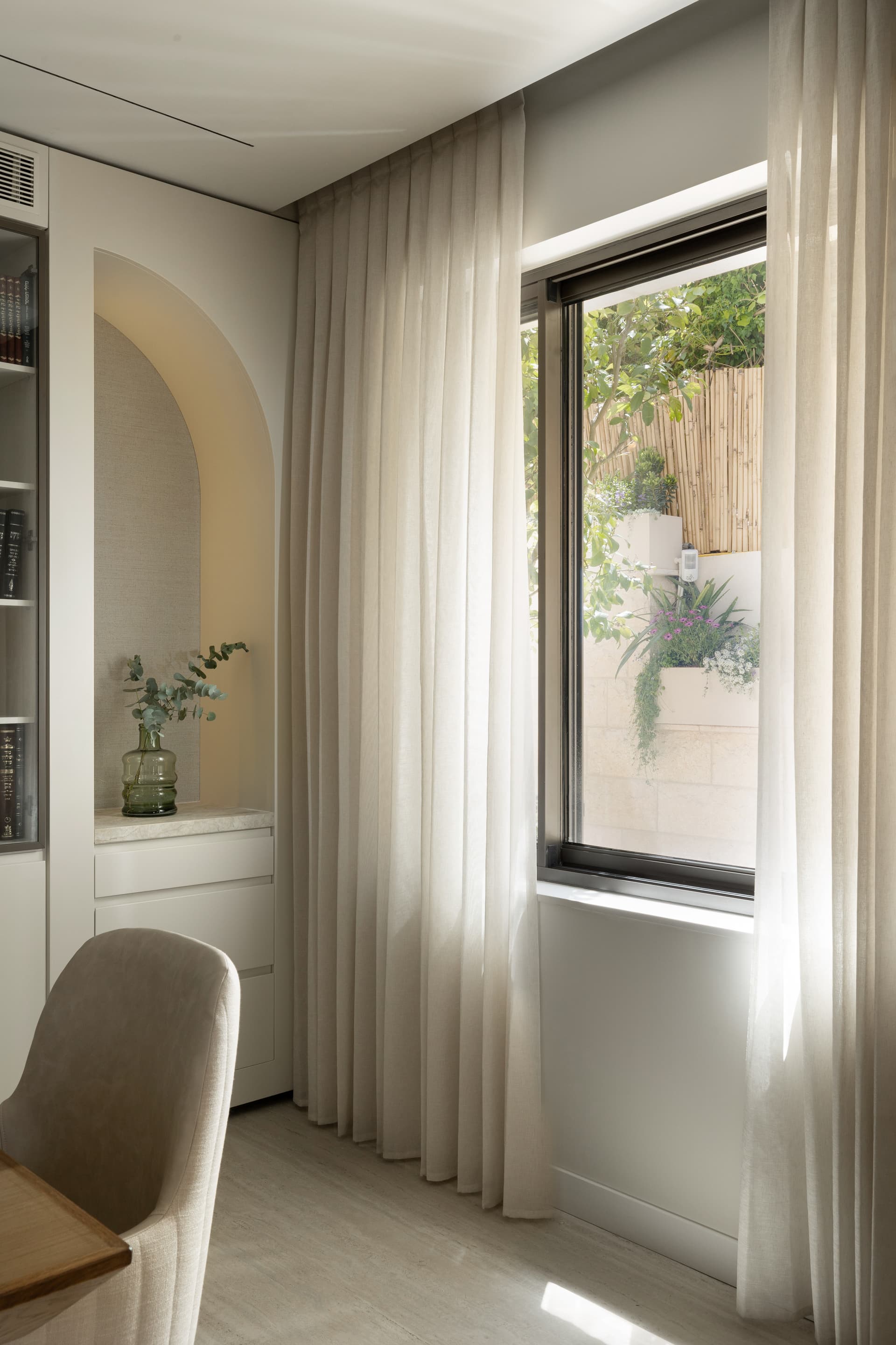 Arched display niche with eucalyptus vase and sheer curtains beside a planted courtyard window