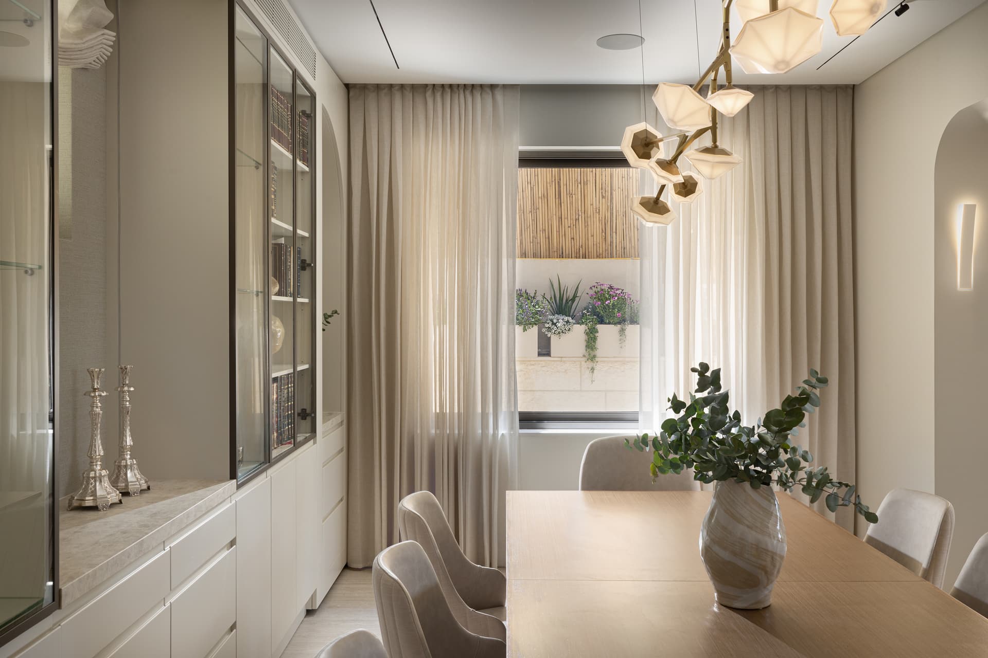 Dining corner with glass-front cabinet, heirloom silver candlesticks, and sheer-filtered window light