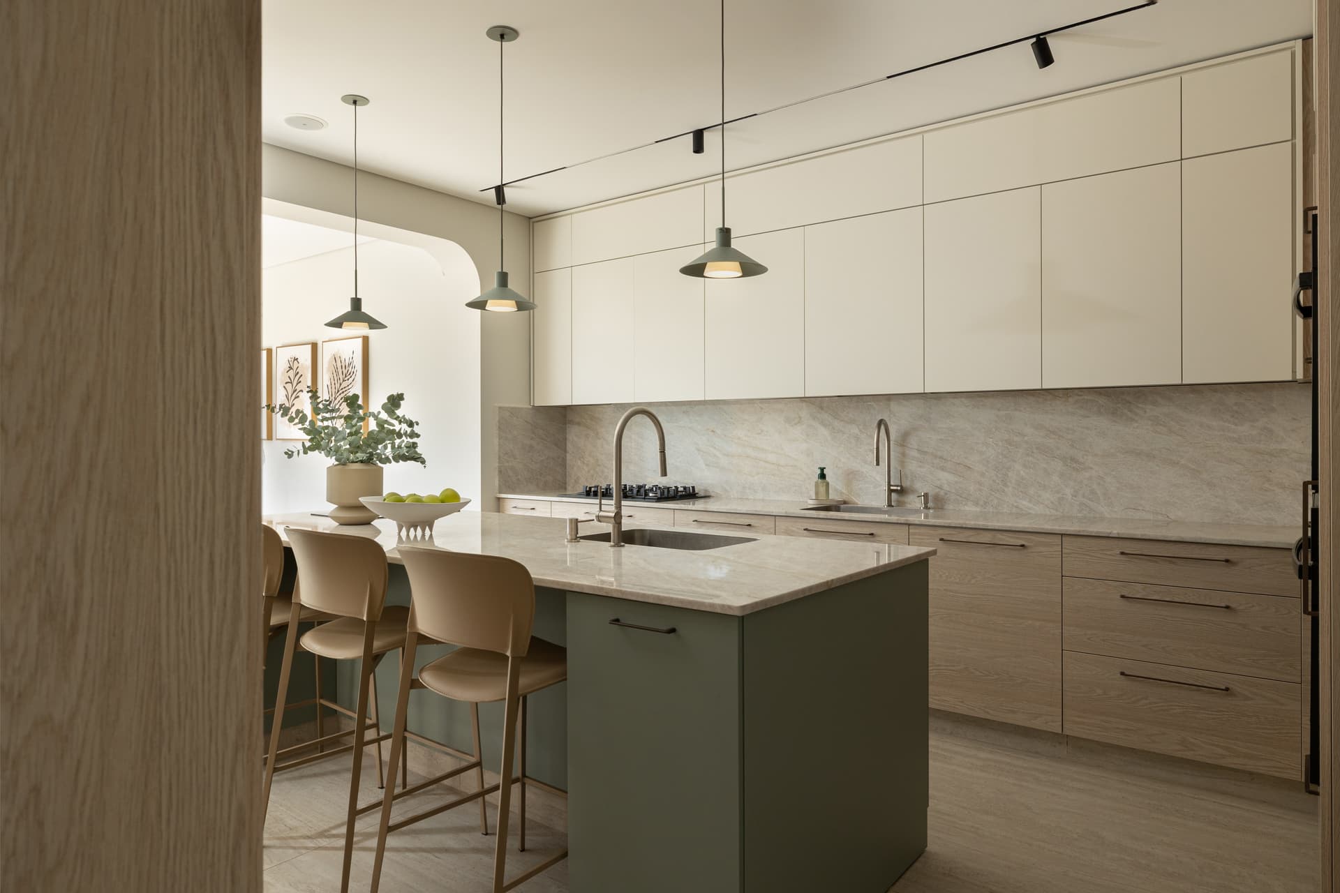 Kitchen with sage-green island, stone slab backsplash, twin faucets, and cream flat-front cabinetry