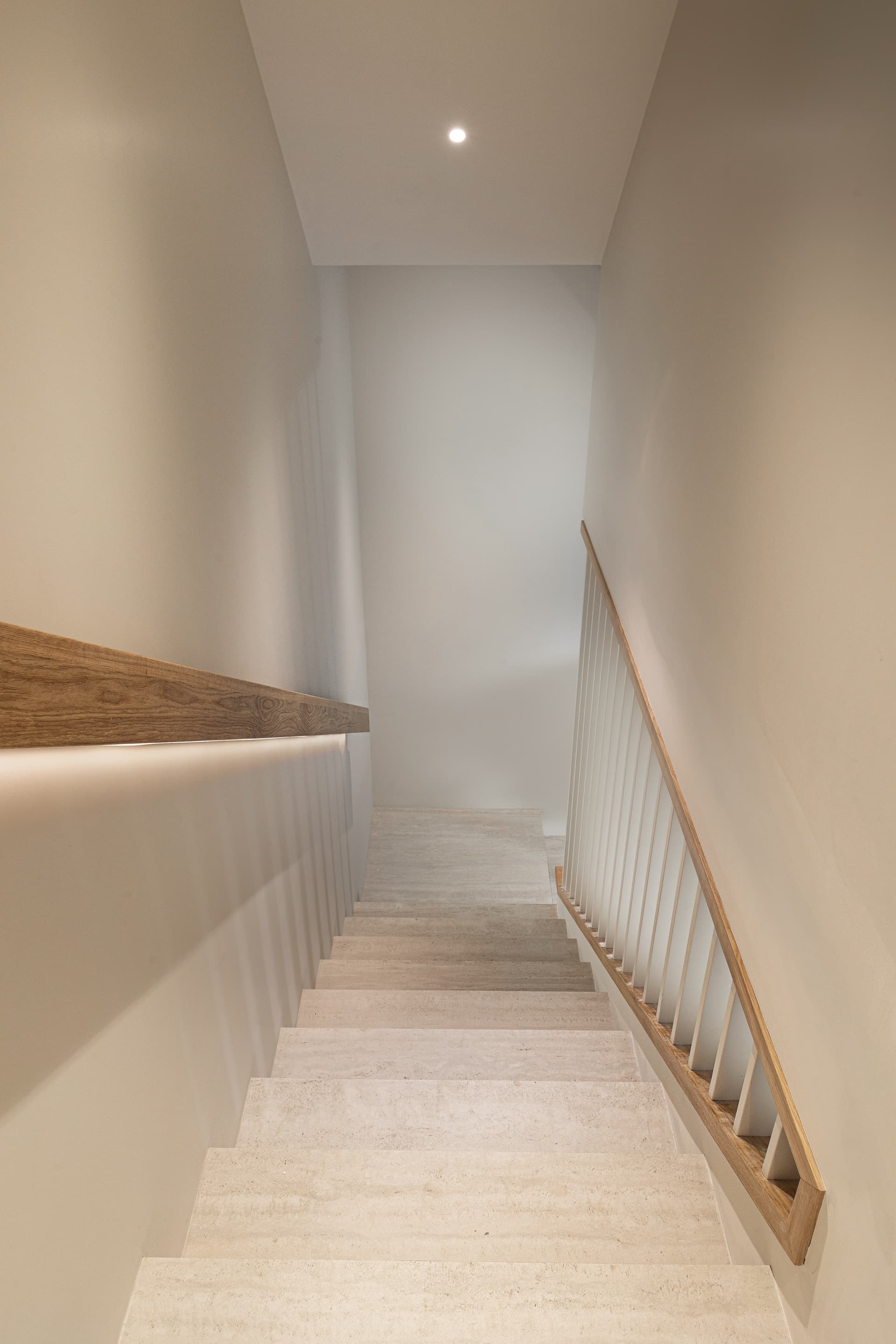 View down the travertine staircase with oak handrail and white spindles