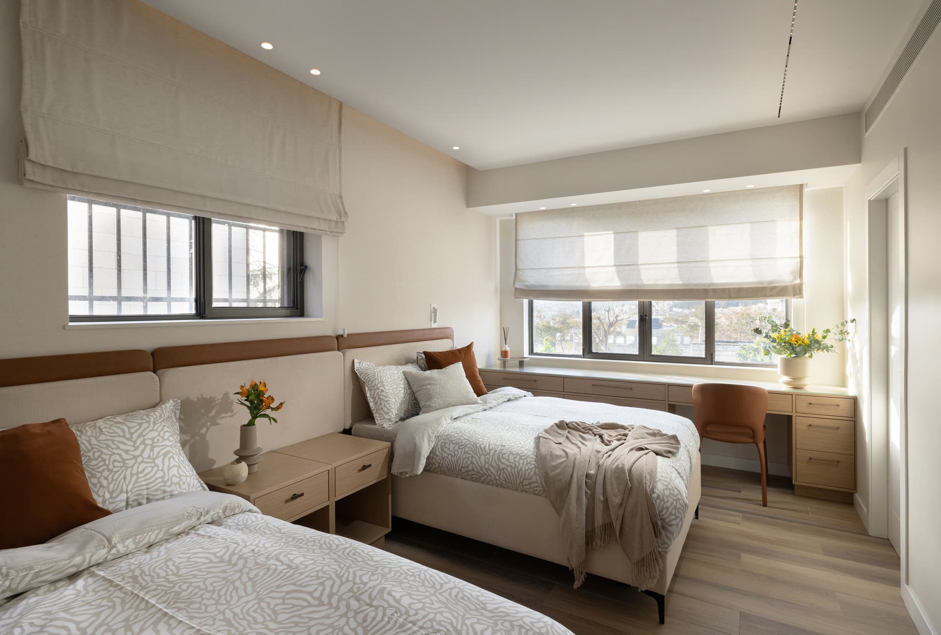 Guest bedroom in golden afternoon light with two beds, window desk, and terracotta accents