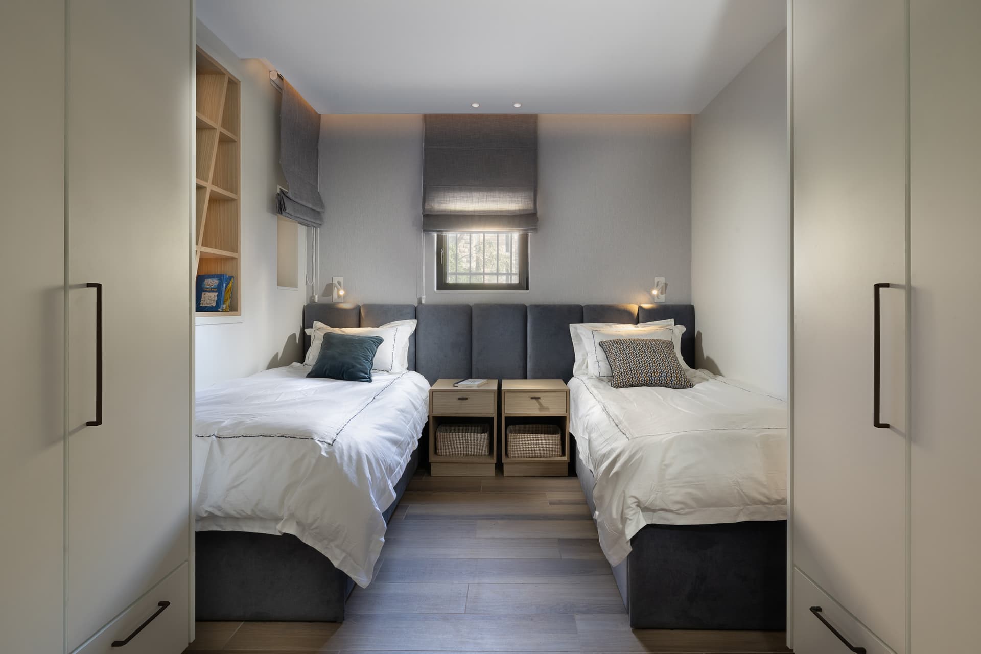 Twin bedroom with symmetrical grey upholstered headboards and roman shades