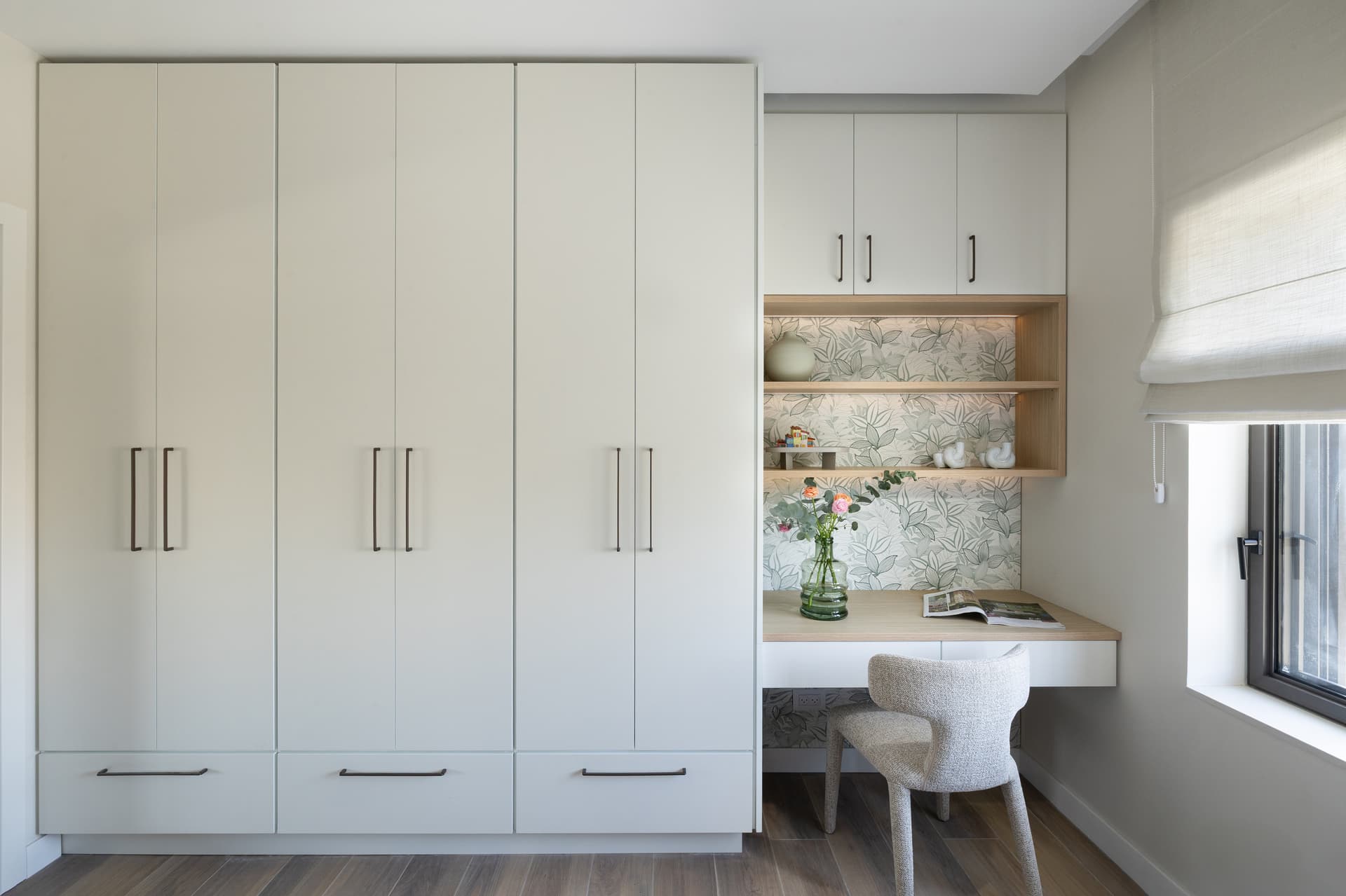 Home office with full-height white wardrobes and an oak desk nook framed by botanical wallpaper