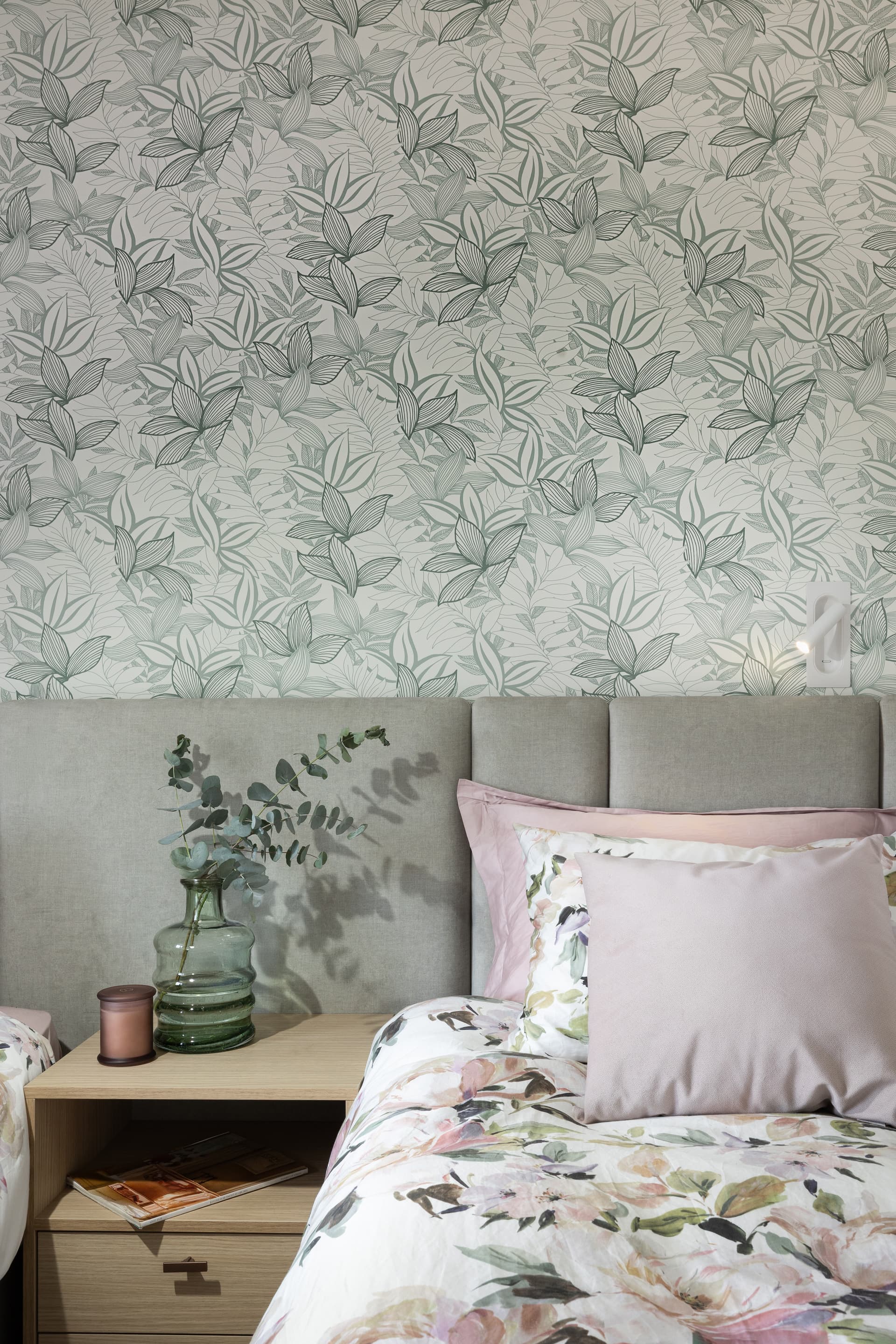 Bedroom with sage leaf wallpaper, channel-stitched headboard, eucalyptus on an oak nightstand, and floral bedding
