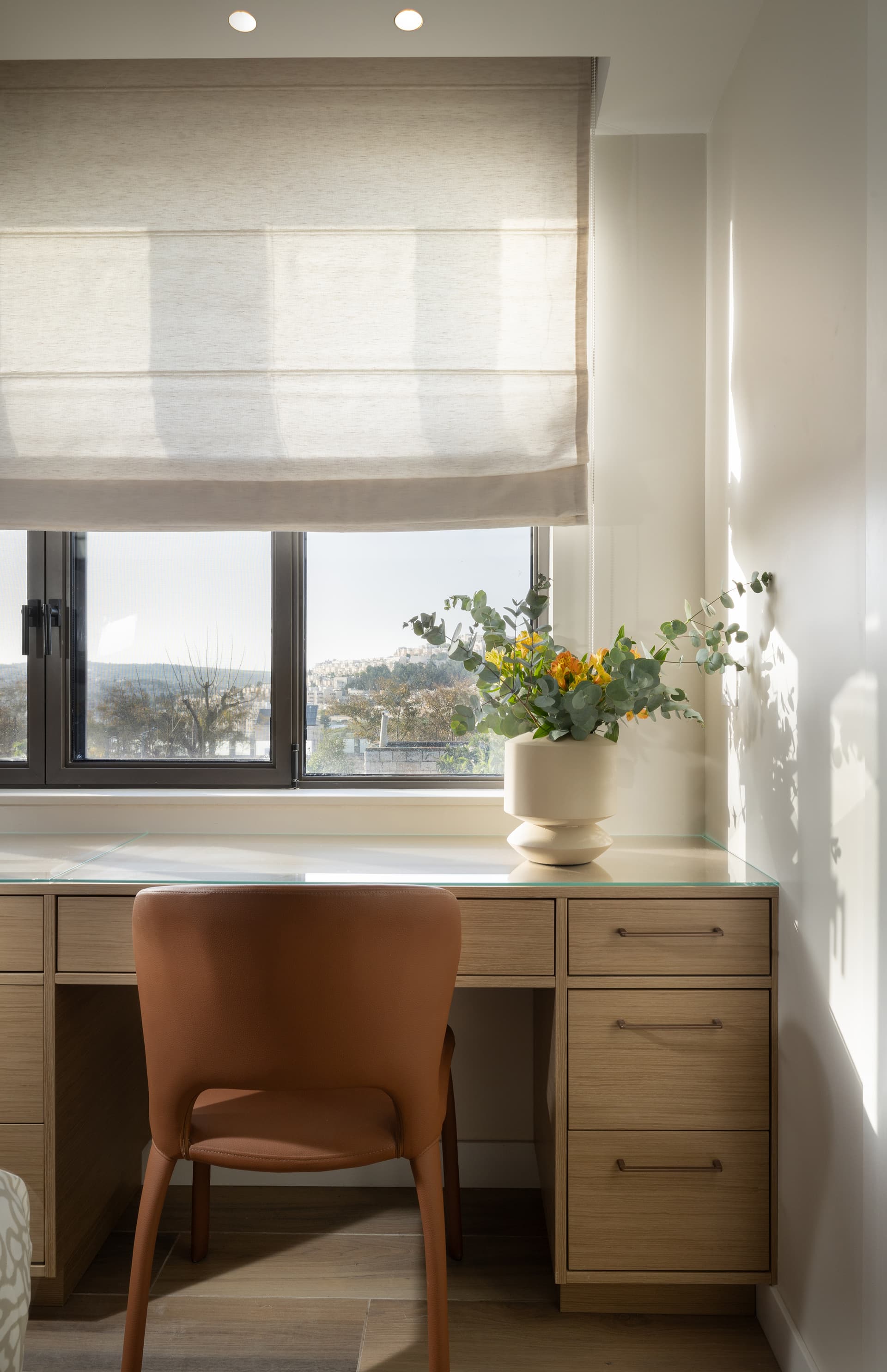 Writing desk at the window with views over Jerusalem, terracotta leather chair, and fresh flowers