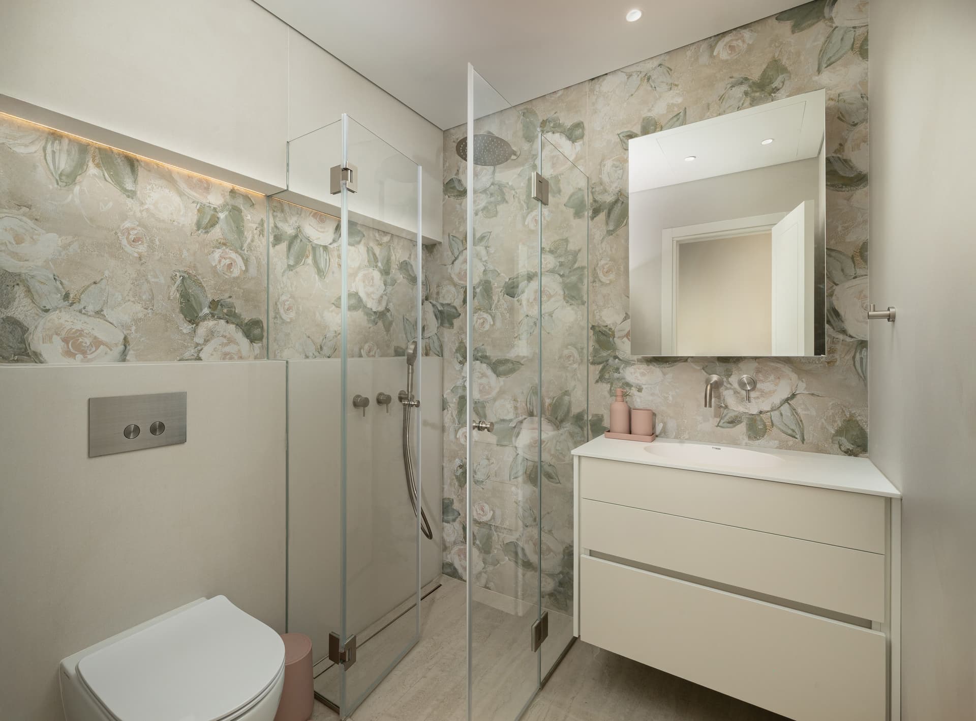 Bathroom with rose-print wall covering, glass shower, and white vanity