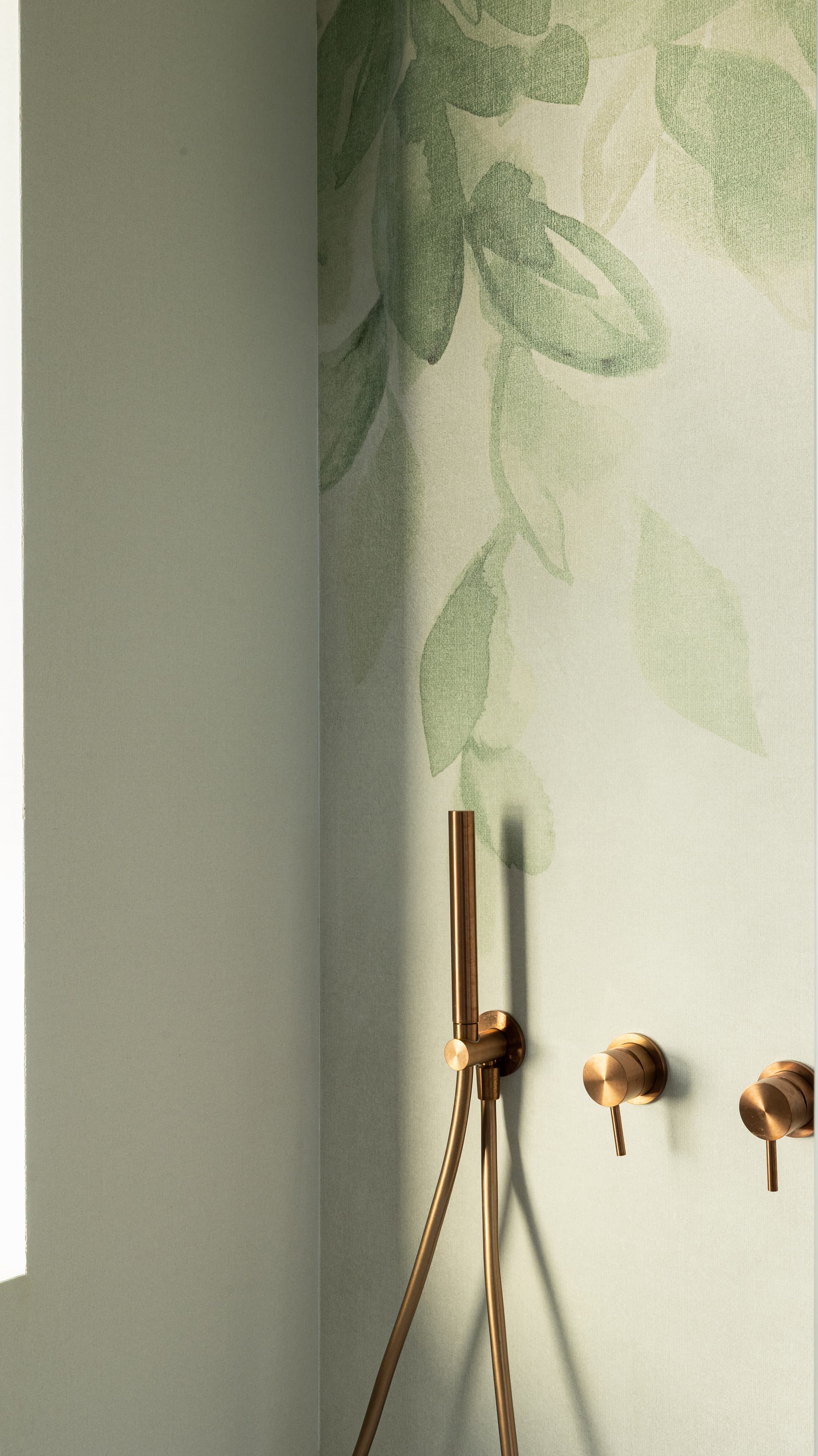 Brushed-copper shower fittings against a sage and leaf-print wall