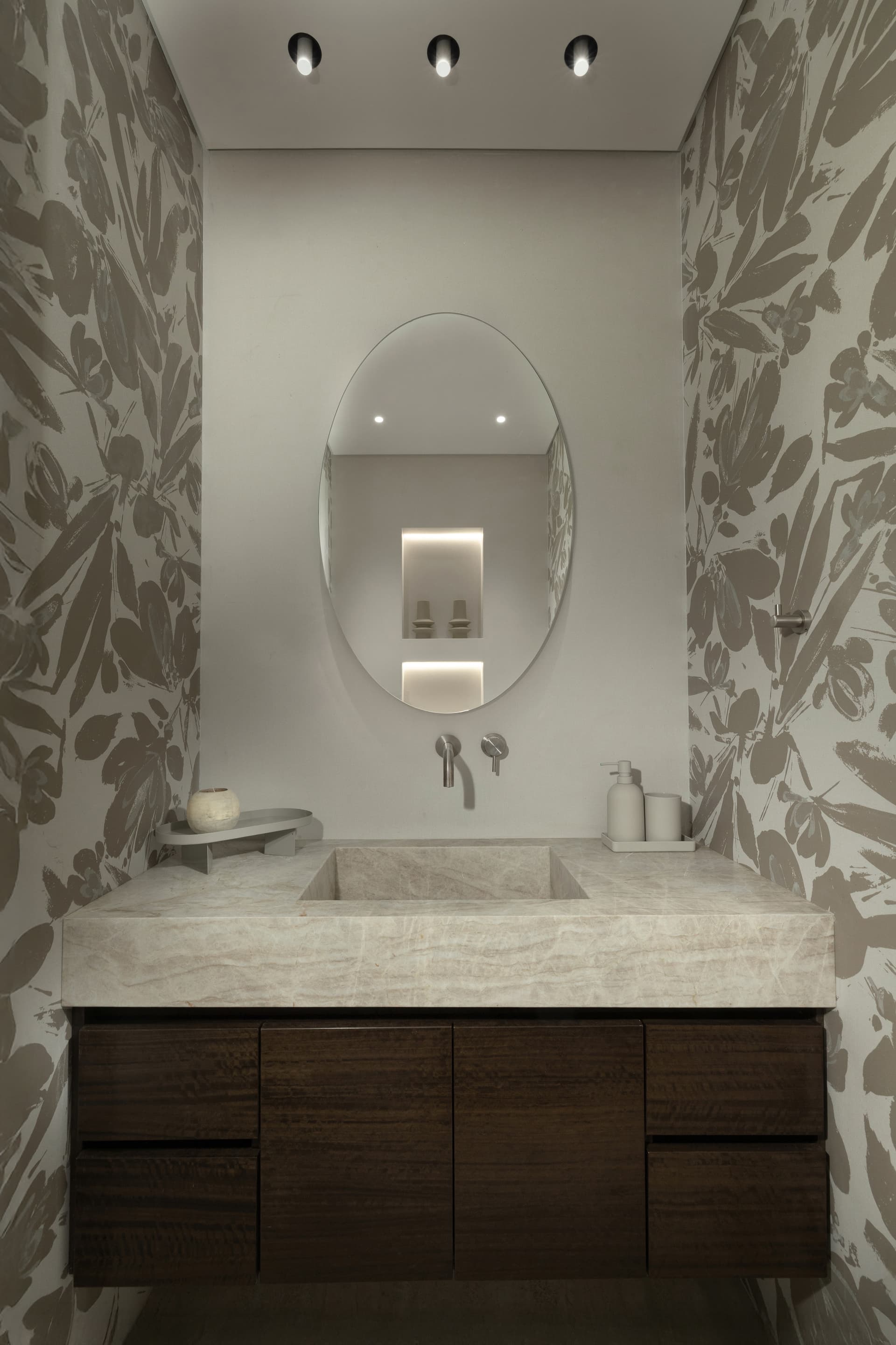 Guest powder room with oval mirror, sculpted stone basin, walnut vanity, and floral wallpaper